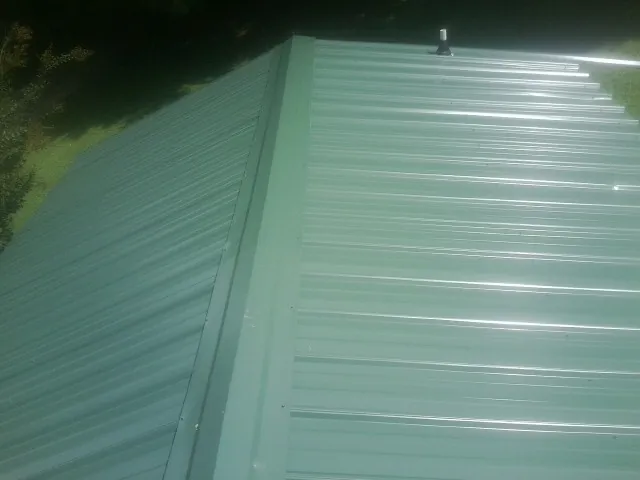 New green metal panels meeting at the ridge of a roof — Flat Roof Repair work by our crew in Lenox